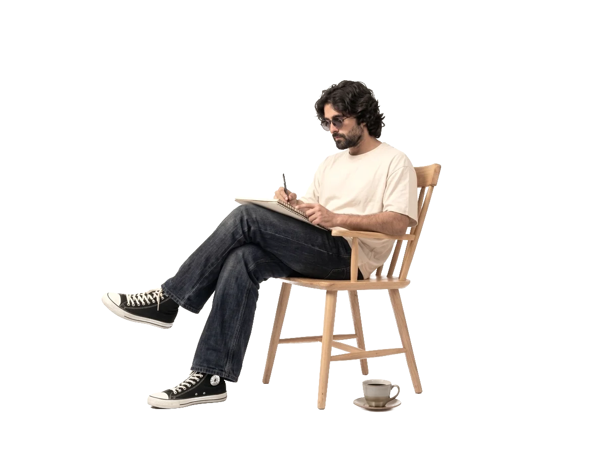 Sketching in a notebook, cross-legged on a wooden chair.